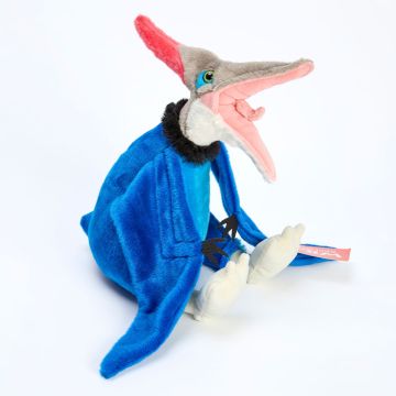 A side view of the Pteranodon Soft Toy sitting with its blue wings draped around its legs and its beak open. 