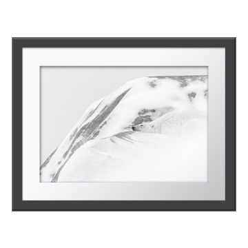 At One with the World Wall Print in a grey frame. A polar bear, almost camouflaged, nestled in a snowdrift against a grey rock face.