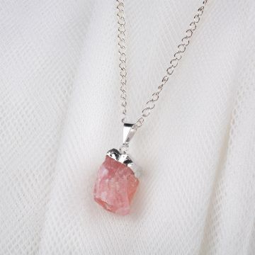 A close up of the rose quartz pendant on a white cloth background, showing the pale pink colour and rough texture of the cube-shaped rock.
