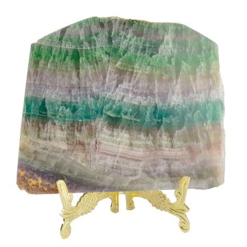 The square-shaped slice is positioned on a gold-coloured stand for styling purposes. The different coloured layers include strips of green, colourless, blue and brown.