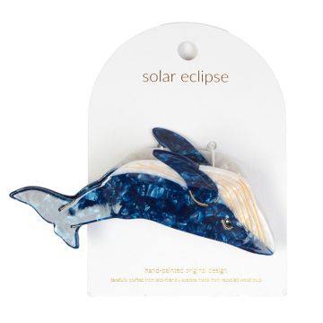 The blue whale shaped hair claw displayed on its packaging. The whale is upside down with its white belly, blue flippers and blue topside.