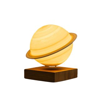 The Saturn lamp tilts to the left as it glows with warm, yellow light and hovers just above the square, wooden base.