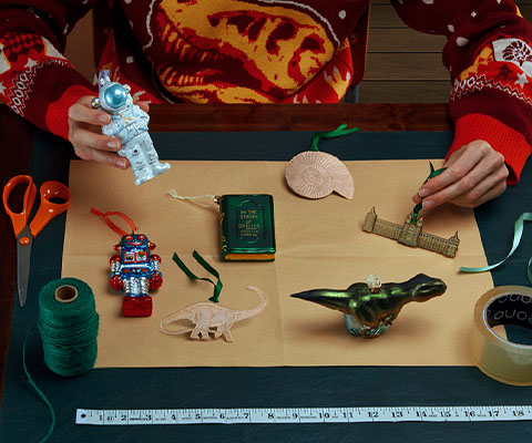 The arms of someone dressed in our Christmas jumper interacts with the decorations that are laid out on parcel paper, ready to wrap.