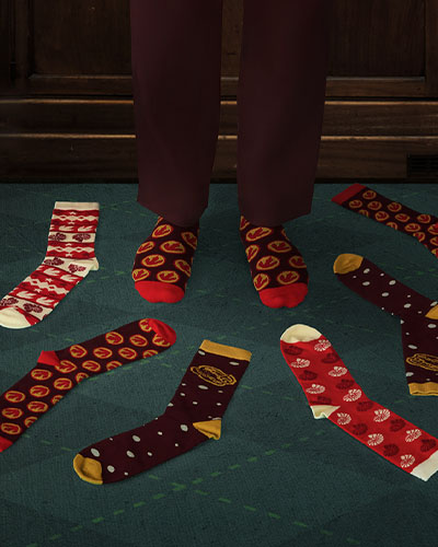 The feet of a person wearing a matching pair of socks are surrounded by other socks with different dinosaur patterns.