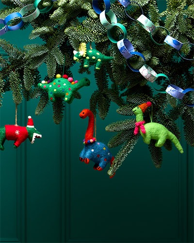 Felt decorations in the shape of different dinosaurs hang on the Christmas tree branches, next to paper chains.