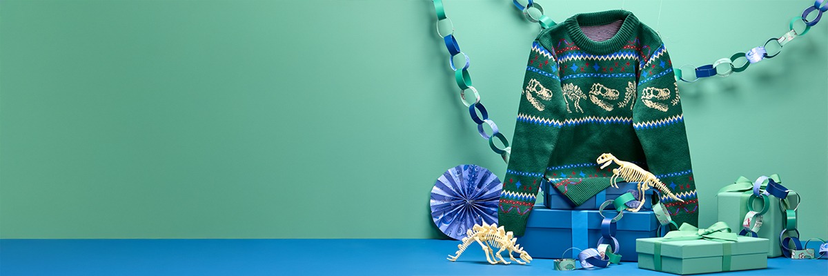 The green Christmas jumper hangs next to paper chains, above gift boxes and dinosaur toys.
