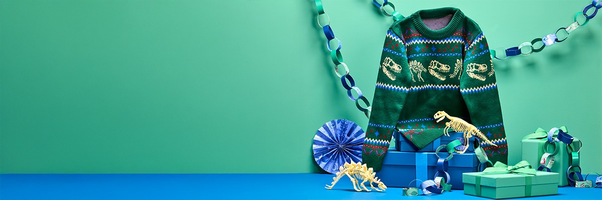 The green Christmas jumper hangs next to paper chains, above gift boxes and dinosaur toys.
