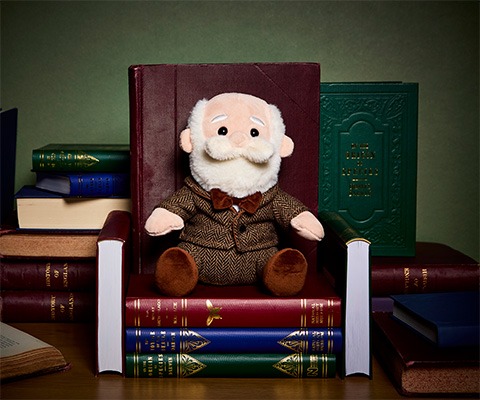 The Charles Darwin Soft Toy is styled sitting on nature-related books that have been shaped into a chair.