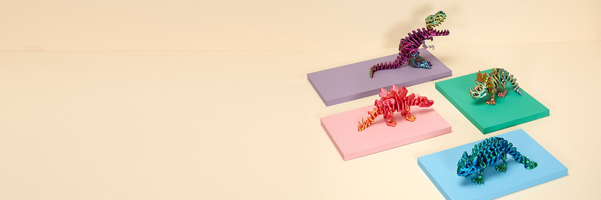 Four dinosaur fidget toys displayed, each on a different coloured mat. They are T. rex, Triceratops, Ankylosaurus and Stegosaurus.
