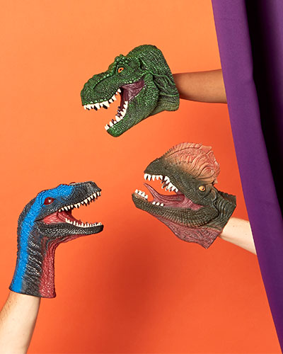 Three dinosaur head hand puppets appear from behind a curtain.