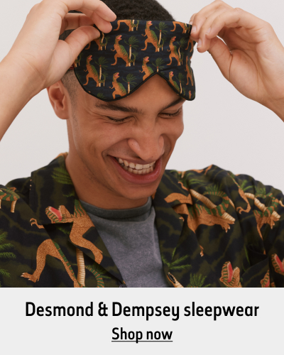 A person wearing a dinosaur patterned eye mask and matching pyjamas. The text reads 'Desmond & Dempsey sleepwear. Shop now'.